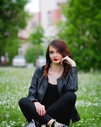 A young Bosnian woman sitting on the grass with dandelions around her in the park